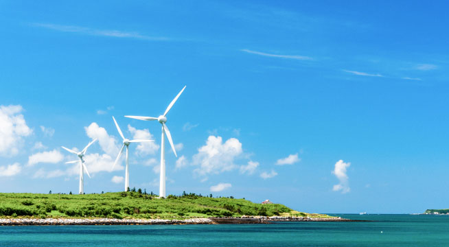 Green hills with huge wind power plants running on a clear sky with clouds in the background