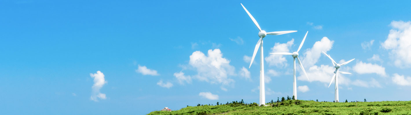 Green hills with huge wind power plants running on a clear sky with clouds in the background